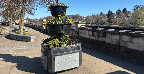 Scottish Water donated planters to Beautiful Perth last year to help brighten up the city centre. A three tiered planter sits in the forefront filled with colouring flowers. Blue sky is overhead.