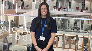 Apprenticeship Week Holly Henderson  Trainee Manager Holly Henderson in front of a glass awards cabinet promoting Apprenticeship Week