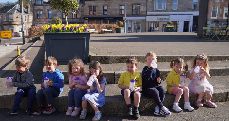 Nursery Children sitting on steps near Top Up Tap, drinking water