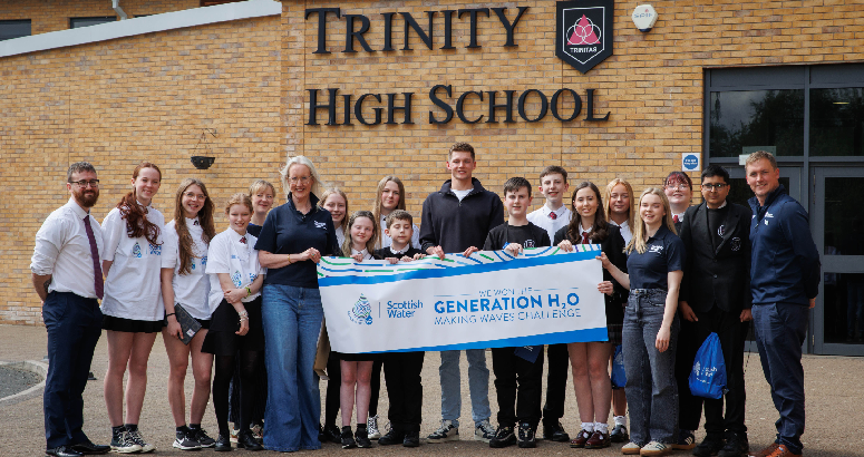 Trinity High School Celebrates Generation H₂O Challenge Win Group photo of students and staff standing outside Trinity High School holding a banner that reads 'Scottish Water - We won the Generation H₂O Making Waves Challenge'. Everyone is smiling and facing the camera.