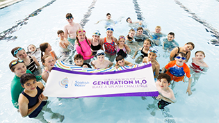 Generation H2O Make a Splash Winning Class children in a pool holding a Generation H2O banner a winners of the Make a Splash Challenge