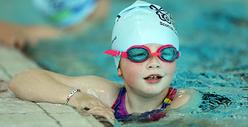 Learn to Swim Partnership 200K Milestone young girl with goggles and swim hat on in pool at poolside