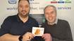 Clive Duncan, Communications Manager, and David Pascall, Project Manager with Thank You Card from Customer Two individuals standing in front of a Scottish Water banner, one holding a Thank You card from a customer with an image of a highland cow on it.