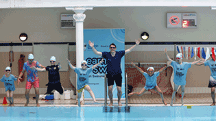 children with teacher at edge of swimming pool