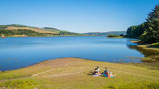 Summer Water Safety Carron Valley reservoir with group of people sunbathing on the shore